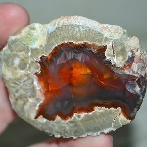 May include: A geode with a large, orange and brown agate crystal inside. The exterior of the geode is a light gray with a rough texture.