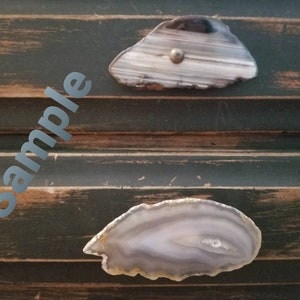 May include: Two natural agate drawer pulls with a silver-colored screw on a distressed green cabinet. The agate pulls are gray, white, and brown with a polished finish. The word "sample" is visible in the image.