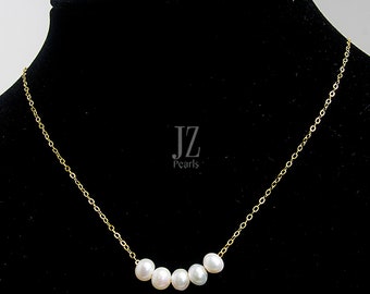 May include: A gold chain necklace with five white pearls arranged in a curved line. The necklace is on a black background with the text "JZ Pearls" in white.