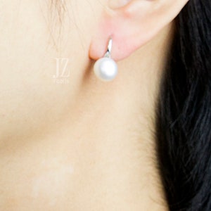 May include: A close-up of a person's ear wearing a silver earring with a white pearl. The pearl is round and smooth.