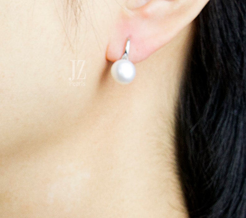 May include: A close-up of a person's ear wearing a silver earring with a white pearl. The pearl is round and smooth.