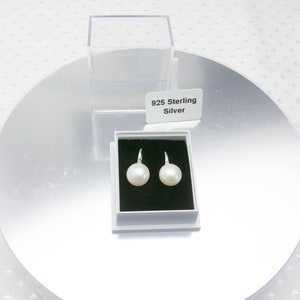 May include: A pair of white pearl earrings with sterling silver hooks in a white box with a black interior. The box has a label that reads "925 Sterling Silver".