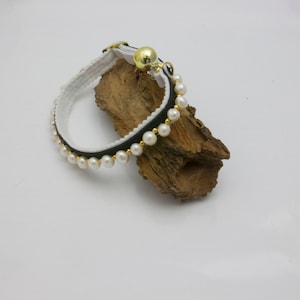 May include: A black and white cat collar with a row of white pearls and a gold bell.