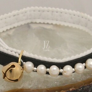 May include: Black leather cat collar with a white velvet lining and a row of white pearls. The collar has a gold bell attached.