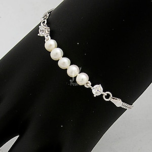 May include: A silver bracelet with a chain and white pearls. The bracelet features a clear crystal accent.