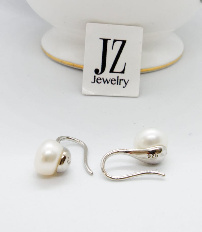 May include: A pair of silver dangle earrings with a white pearl on each earring. The earrings are marked with "925" on the back.