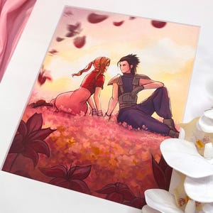 May include: A framed art print featuring a couple in a field of flowers. The artwork depicts a man and woman sitting together, surrounded by pink and red flowers. The color palette includes pink, red, and orange hues, with a white mat and frame.
