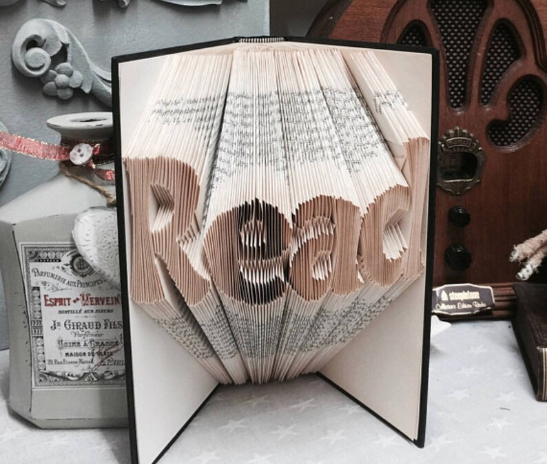 May include: A book with pages folded to form the word Read in a three-dimensional style. The book has a black cover and white pages with black printed text. The folded pages create a sculptural effect, standing upright with the word clearly visible.