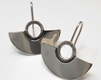 May include: A pair of silver earrings with a half-circle design and a textured circle in the center.