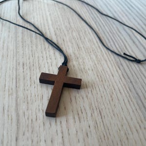 May include: A wooden cross pendant on a black cord necklace. The cross is dark brown and has a simple design.
