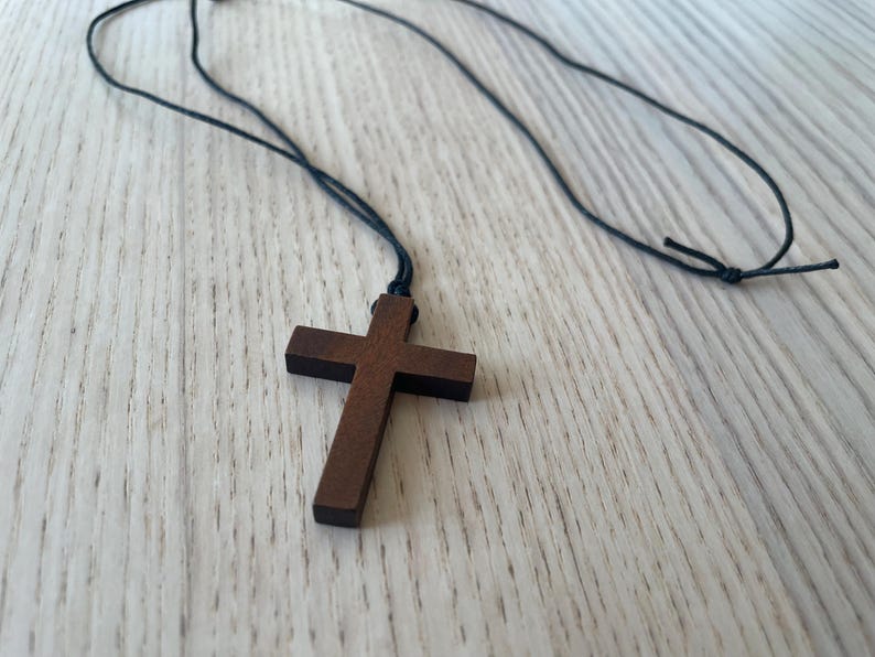 May include: A wooden cross pendant on a black cord necklace. The cross is dark brown and has a simple design.