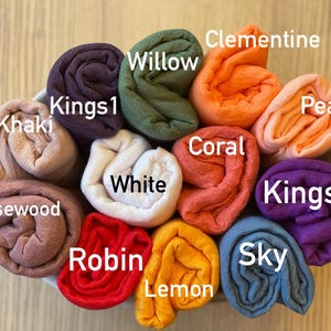 Op de afbeelding: Een verzameling opgerolde stoffen in verschillende kleuren, waaronder Khaki, Kings1, Willow, Clementine, Perzik, Kings2, Sky, Citroen, Robin, Rozenhout, Wit en Koraal. Elke stof is gelabeld met zijn kleurnaam.