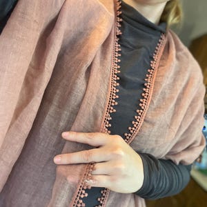 May include: A dusty rose scarf featuring a delicate, scalloped lace trim along the edges. The lightweight fabric has a subtle, semi-sheer texture, and the decorative border consists of small, repeating circular motifs that frame the scarf's length.