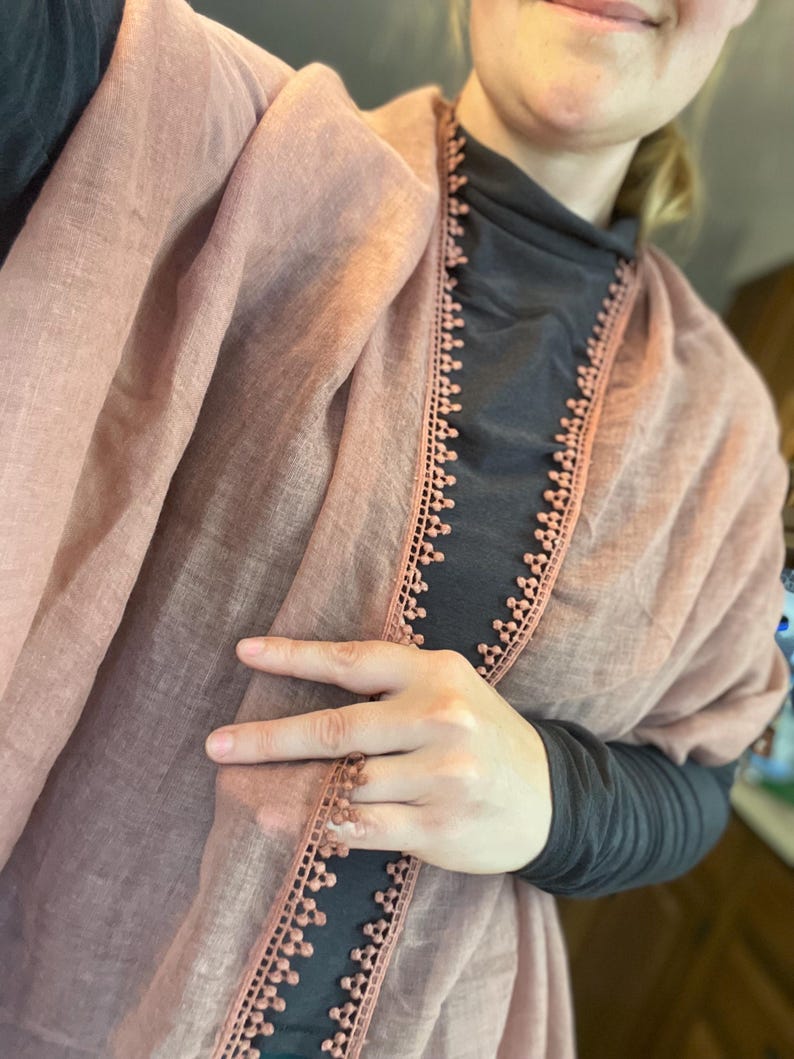 May include: A dusty rose scarf featuring a delicate, scalloped lace trim along the edges. The lightweight fabric has a subtle, semi-sheer texture, and the decorative border consists of small, repeating circular motifs that frame the scarf's length.