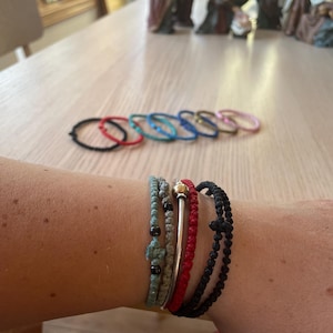 May include: A close-up of a person's wrist wearing several bracelets. The bracelets are made of different materials, including string, metal, and beads. The bracelets are in various colours, including black, red, blue, and green.