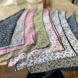 May include: A collection of floral patterned fabric bandanas in various colors, including navy, gray, pink, green, white, and blue. Each bandana has a decorative lace trim along the edge. The bandanas are arranged in a fan shape.