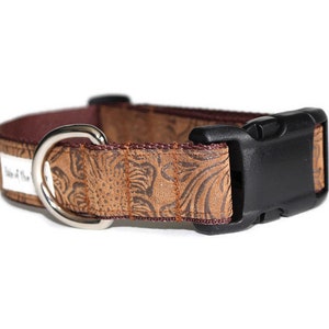 May include: A brown dog collar with a floral embossed pattern and a black plastic buckle. The collar has a silver D-ring.