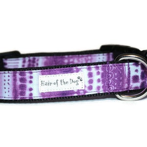 May include: Purple and white patterned dog collar with black edging and a silver D-ring. The collar has a white label that reads "Hair of the Dog".