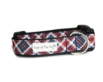 May include: Red, white, and blue plaid dog collar with a black border and a silver D-ring. The collar has a white label with the text "Hair of the Dog" in black.