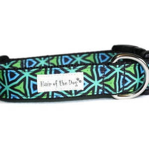 May include: A green, blue, and black patterned dog collar with a silver D-ring and a black buckle. The collar has a white label that says "Hair of the Dog".
