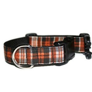 May include: A black and orange plaid dog collar with a silver metal D-ring and a black plastic buckle.
