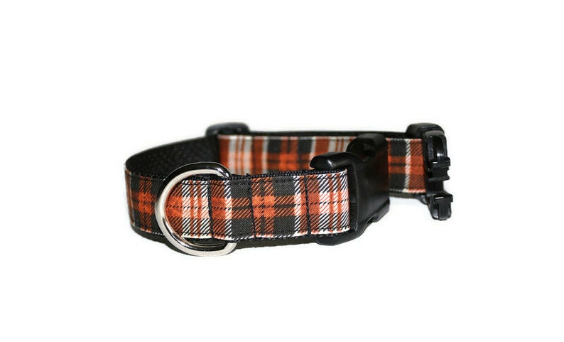 May include: A black and orange plaid dog collar with a silver metal D-ring and a black plastic buckle.