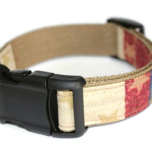 May include: A tan dog collar with a red, white, and blue American flag design. The collar has a black plastic buckle.