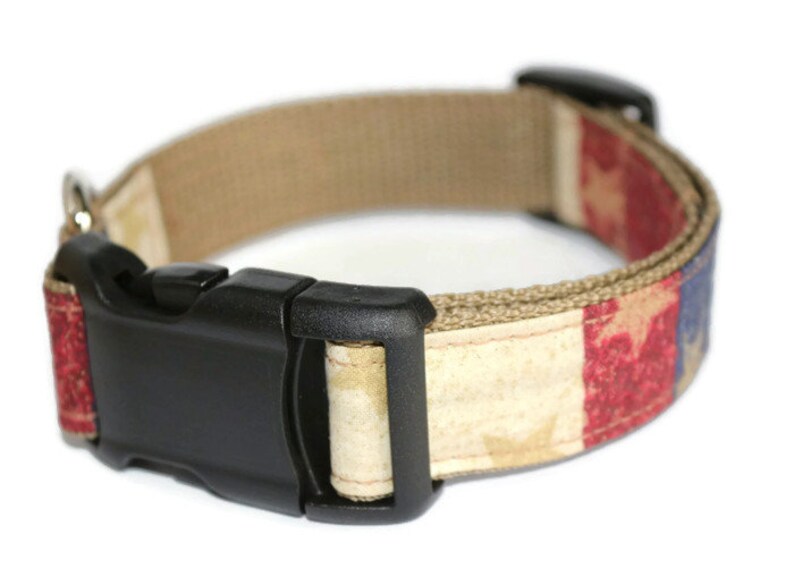 May include: A tan dog collar with a red, white, and blue American flag design. The collar has a black plastic buckle.