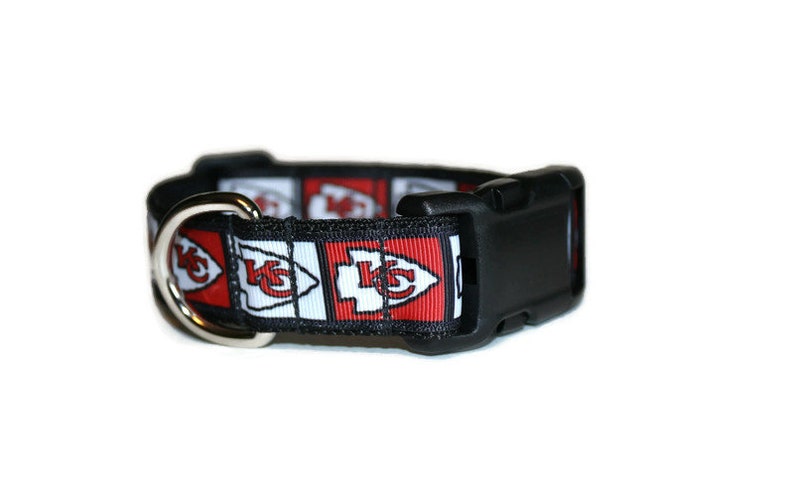 May include: A black dog collar with a red, white, and black patterned ribbon featuring the Kansas City Chiefs logo.