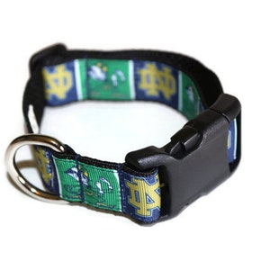May include: A blue, green, and gold dog collar with a black buckle and a silver D-ring. The collar features a repeated pattern of a mascot and the letters "ND".
