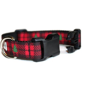 May include: Red and black tartan dog collar with green Christmas trees printed on it. The collar has a black plastic buckle and a silver D-ring.