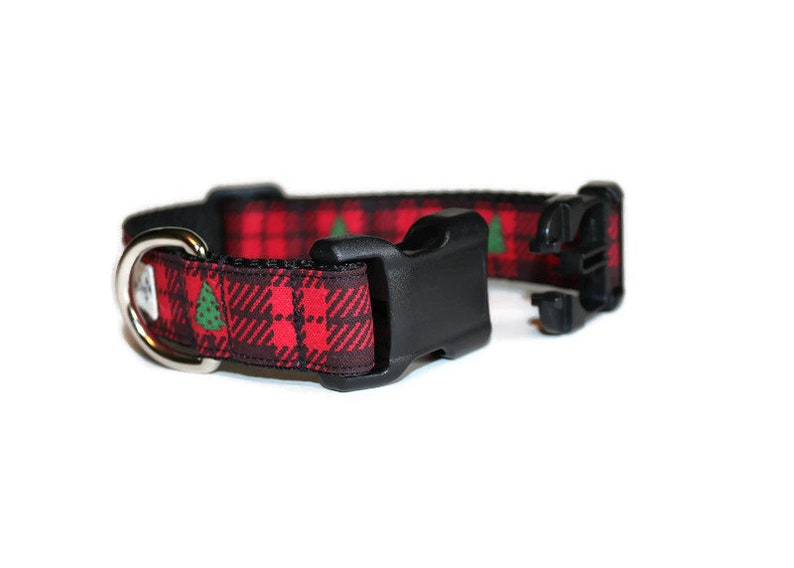 May include: Red and black tartan dog collar with green Christmas trees printed on it. The collar has a black plastic buckle and a silver D-ring.
