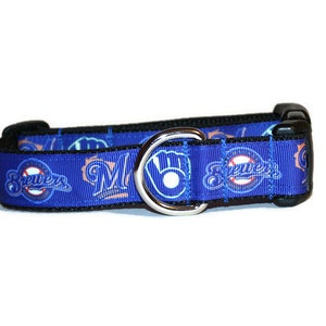 May include: Blue dog collar with a repeating pattern of the Milwaukee Brewers logo, including the team's "M" and "Brewers" text, and a baseball with a glove. The collar has a black buckle and a silver D-ring.