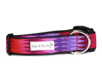 May include: A pink and purple dog collar with a geometric pattern and black trim. The collar has a silver metal D-ring and a white label that reads "Hair of the Dog".