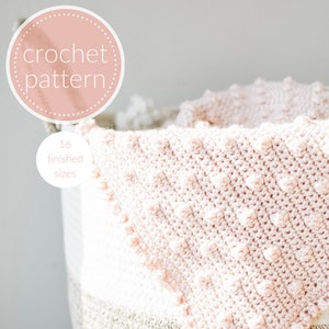 Puede incluir: Una manta de bebé de crochet rosa con un patrón de puntadas texturizadas, doblada y colocada en una cesta tejida. La manta está disponible en 16 tamaños.