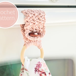 May include: A pink crocheted towel ring with a wooden ring and a brown button. The ring is hanging on a white cabinet door.