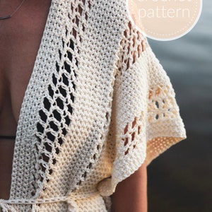 May include: A white crochet cover-up with a V-neck and a tie belt. The cover-up has a delicate openwork pattern and is perfect for layering over a swimsuit.