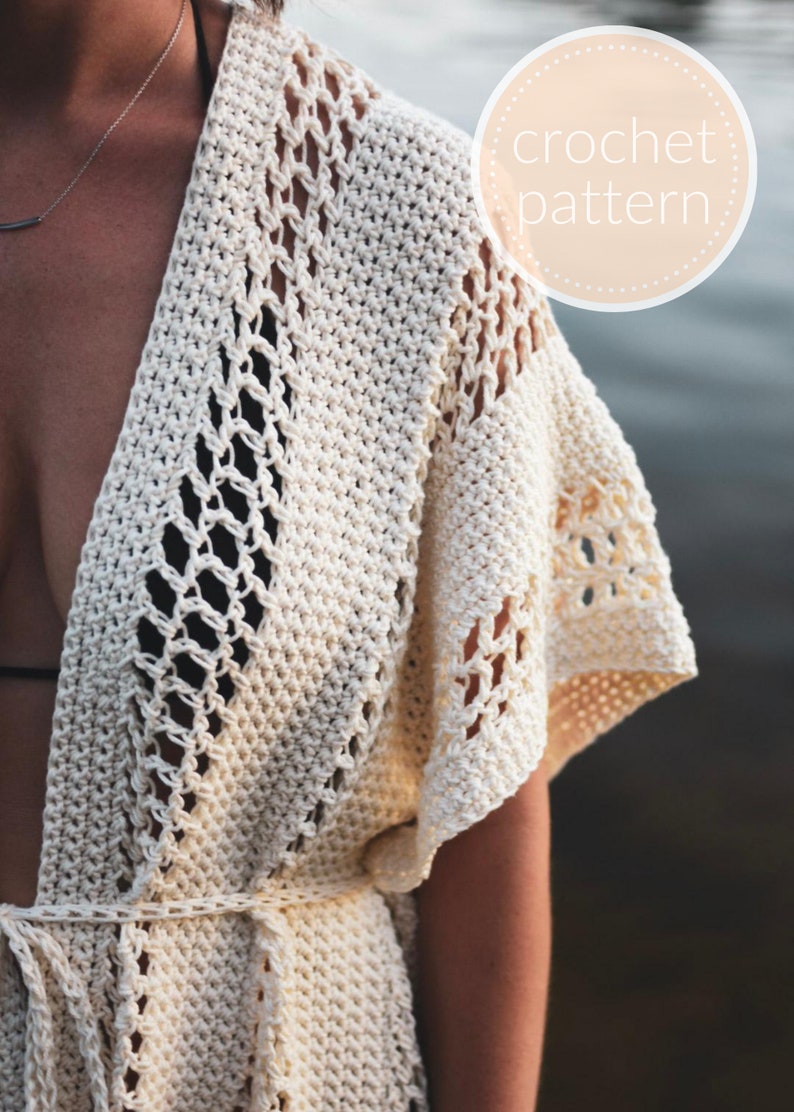May include: A white crochet cover-up with a V-neck and a tie belt. The cover-up has a delicate openwork pattern and is perfect for layering over a swimsuit.