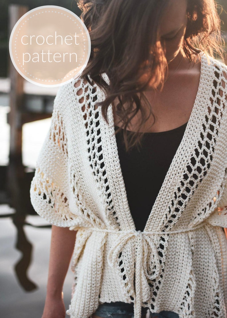 May include: A white crochet cardigan with a tie closure. The cardigan has a delicate openwork pattern and is worn over a black tank top.