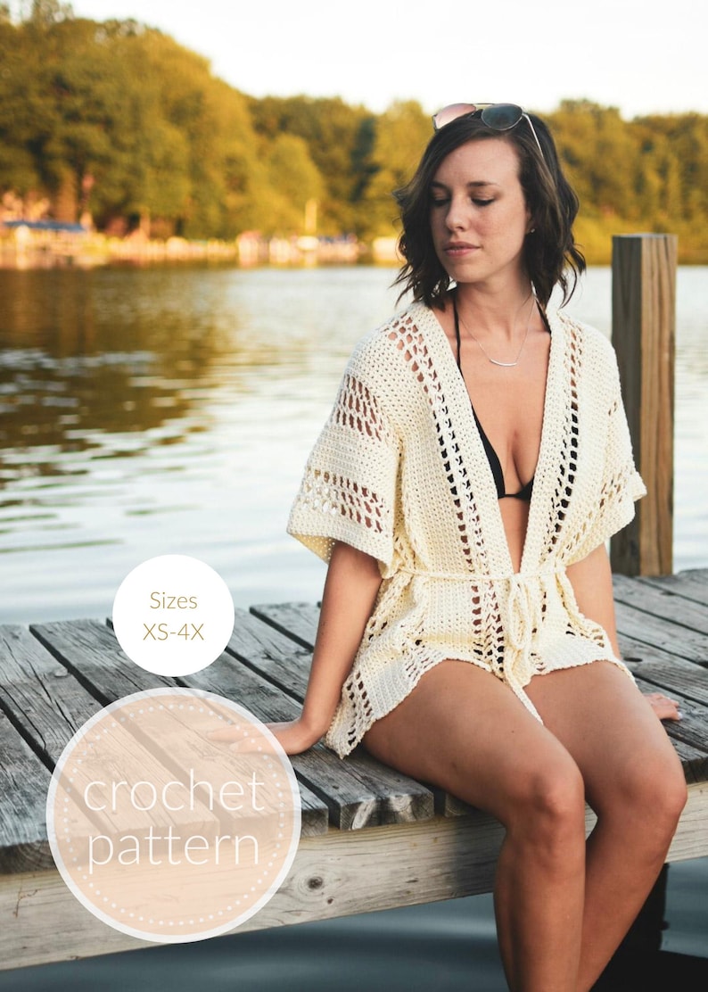 May include: A white crochet cover-up with a tie waist, worn by a person sitting on a wooden dock. The cover-up has a delicate openwork pattern. The text "Sizes XS-4X" and "crochet pattern" are visible in the image.