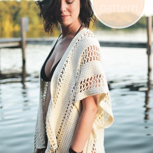 May include: A white crochet cover-up with a lacy design. The cover-up has a V-neck and short sleeves. The model is wearing the cover-up over a black swimsuit.