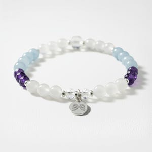 A bracelet with white and purple beads, silver charms, and a winged charm on a white background.