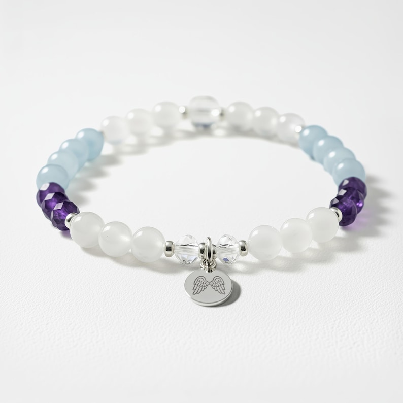 A bracelet with white and purple beads, silver charms, and a winged charm on a white background.