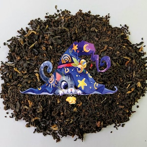 May include: A black tea blend with a whimsical illustration of a cat wearing a witch's hat and holding a glowing orb. The tea is loose leaf and appears to be a blend of black tea and other herbs.