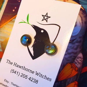 May include: A pair of iridescent green and blue labradorite gemstone earrings on a white card with a black crow illustration and the text "The Hawthorne Witches (541) 205 4238 Etsy: TheHawthorneWitches"