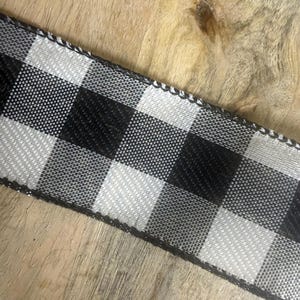 May include: Black and white checkered ribbon with a woven texture. The ribbon features a classic buffalo plaid pattern, with alternating black and white squares. The edges are finished with a black trim.