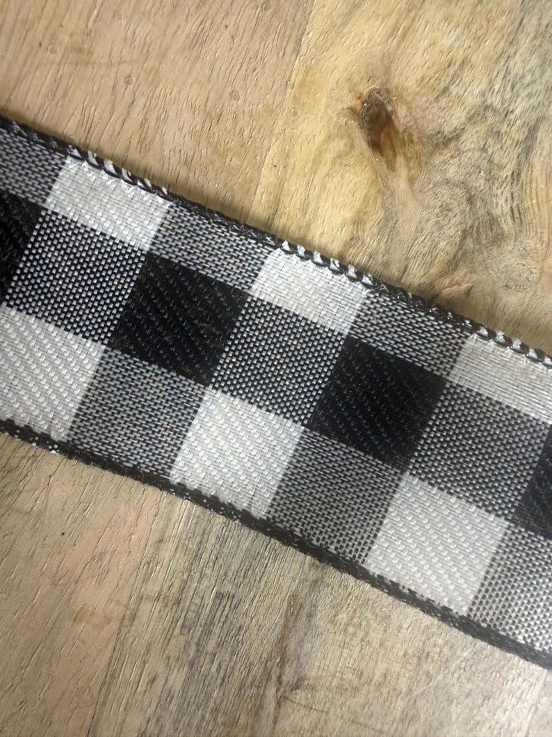 May include: Black and white checkered ribbon with a woven texture. The ribbon features a classic buffalo plaid pattern, with alternating black and white squares. The edges are finished with a black trim.