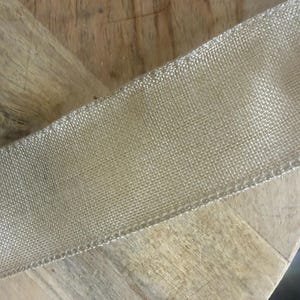 May include: A close-up of a gold mesh ribbon, likely for crafting or decoration. The ribbon has a fine, woven texture and a metallic sheen. The ribbon is positioned diagonally across a wooden surface.