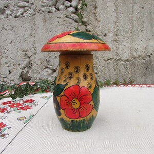 May include: A hand-painted wooden mushroom-shaped container with a red, yellow, and green floral design. The container is closed with a lid that is also painted with a floral design.