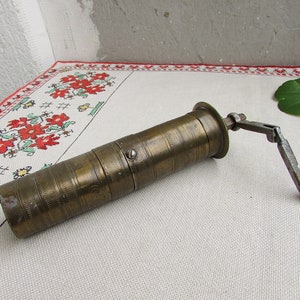Puede incluir: Un molinillo de pimienta vintage de latón con una manivela de metal. El molinillo tiene una superficie texturizada y está en buen estado.